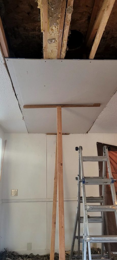 Water-damaged ceiling section cut out with new drywall going up.